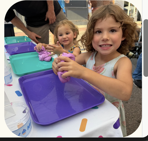 A child squishing purple play dough on a colorful tray at the mixing bar