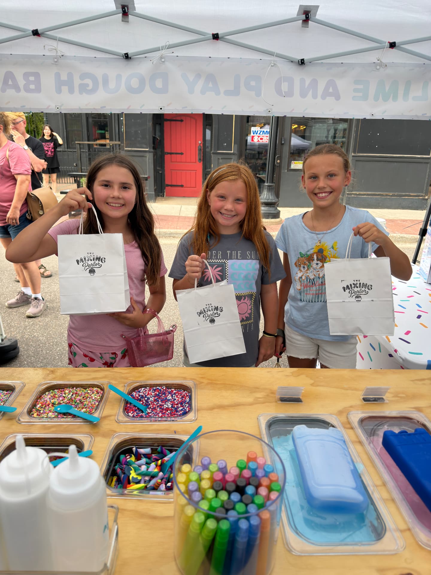 Three kids holding Mixing Parlor take-home bags at a street market pop-up