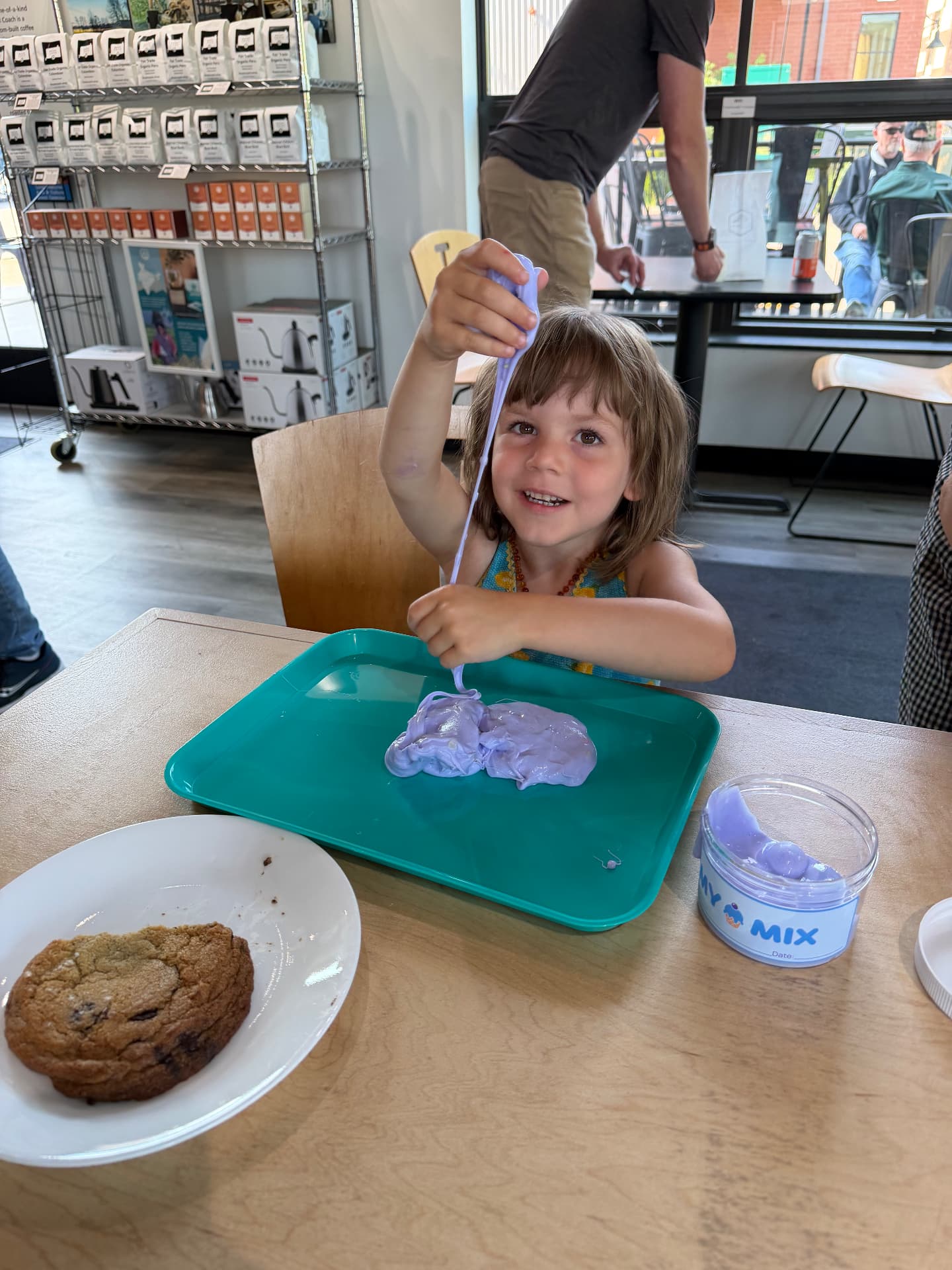 A toddler pulling a drip of lavender slime out of a My Mix cup at a cafe table